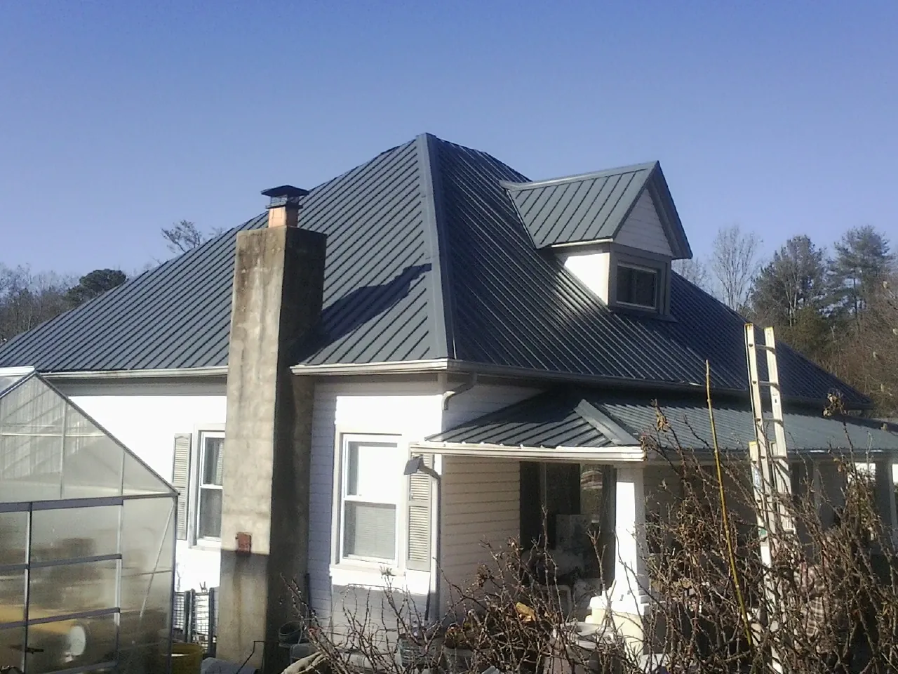 Dark blue standing seam metal roof on a white farmhouse with dormer — Slate & Tile Roof Repair by Roofing Brothers in Otego