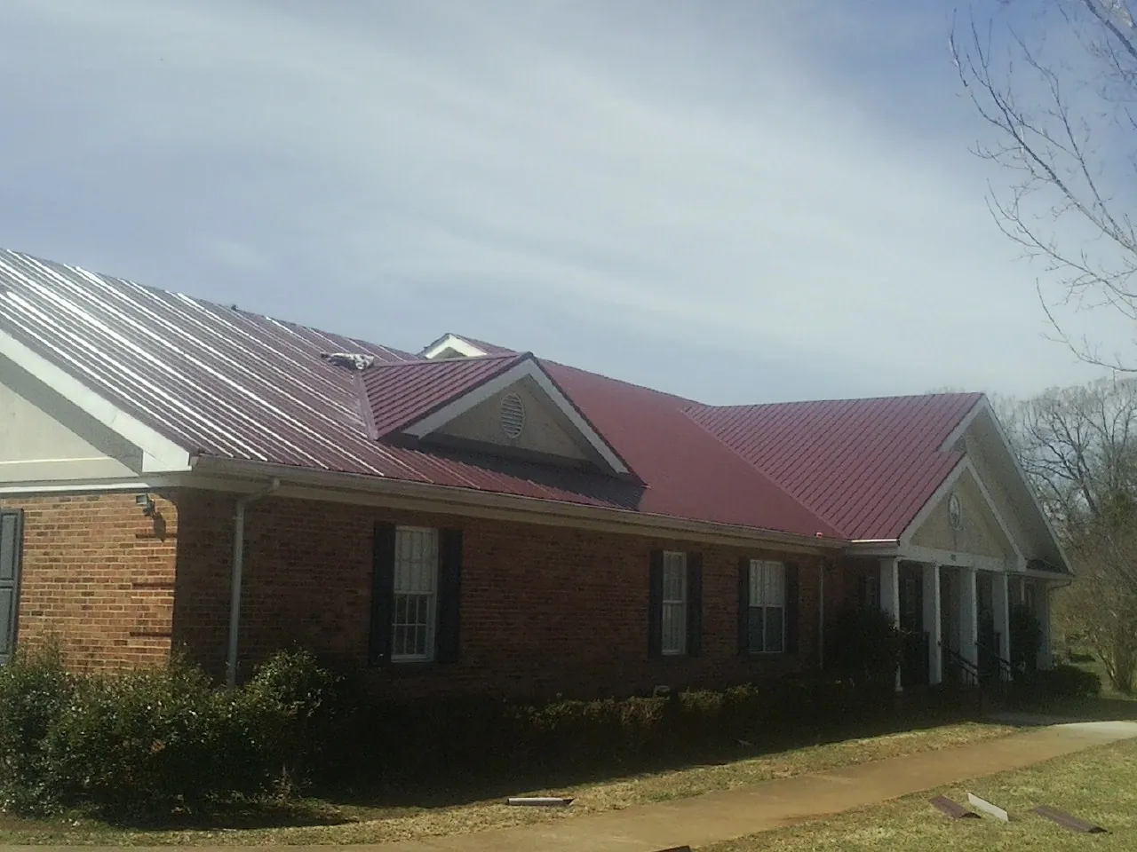 Red metal roof with gabled entries on a long brick building, from a Hail Damage Roof Repair job in Otego