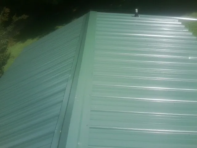 New green metal panels meeting at the ridge of a roof — Flat Roof Repair work by our crew in Otego