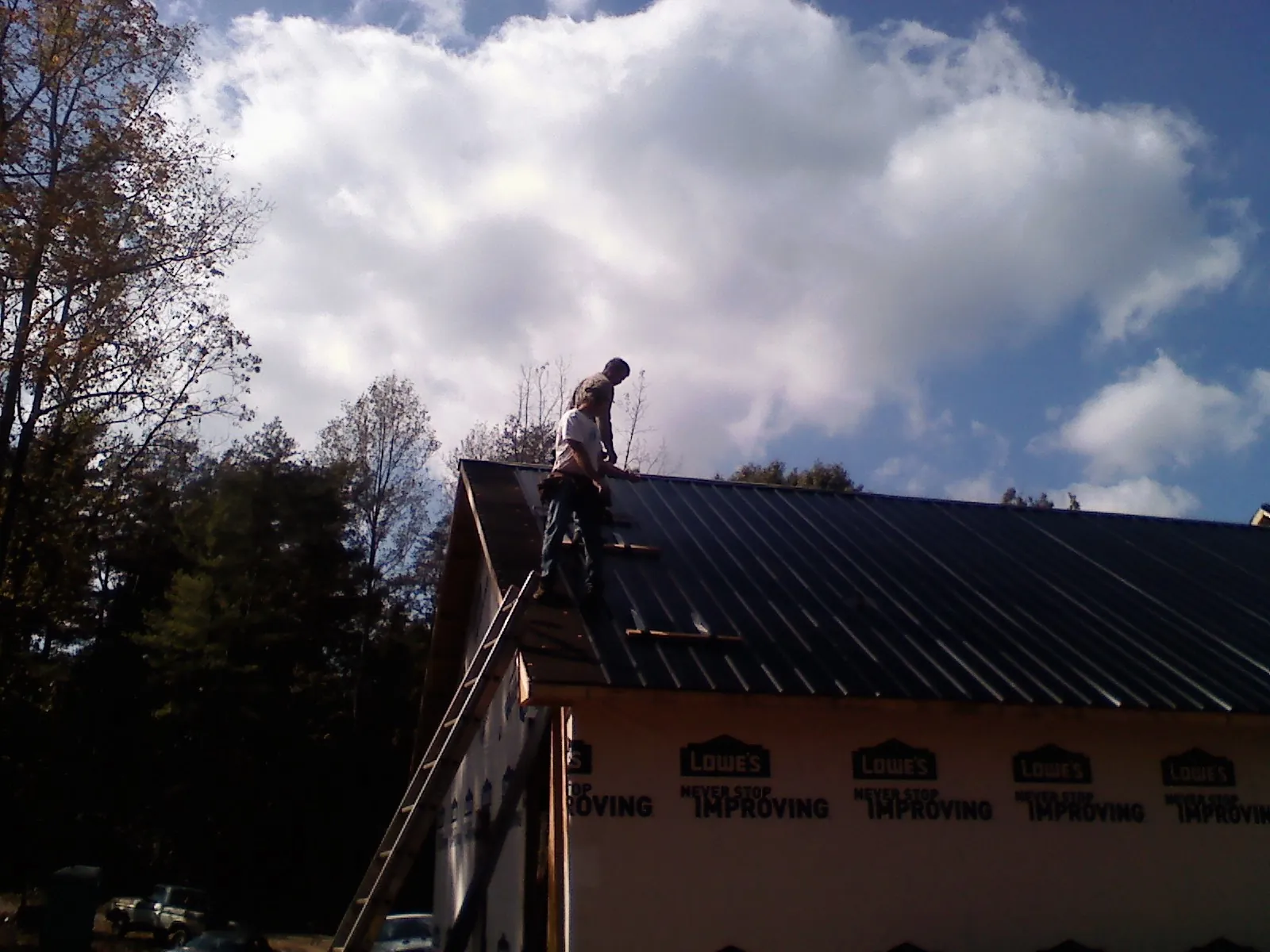 Roofer fastening dark metal panels high against a cloudy sky, from a Roof Inspection job in Otego