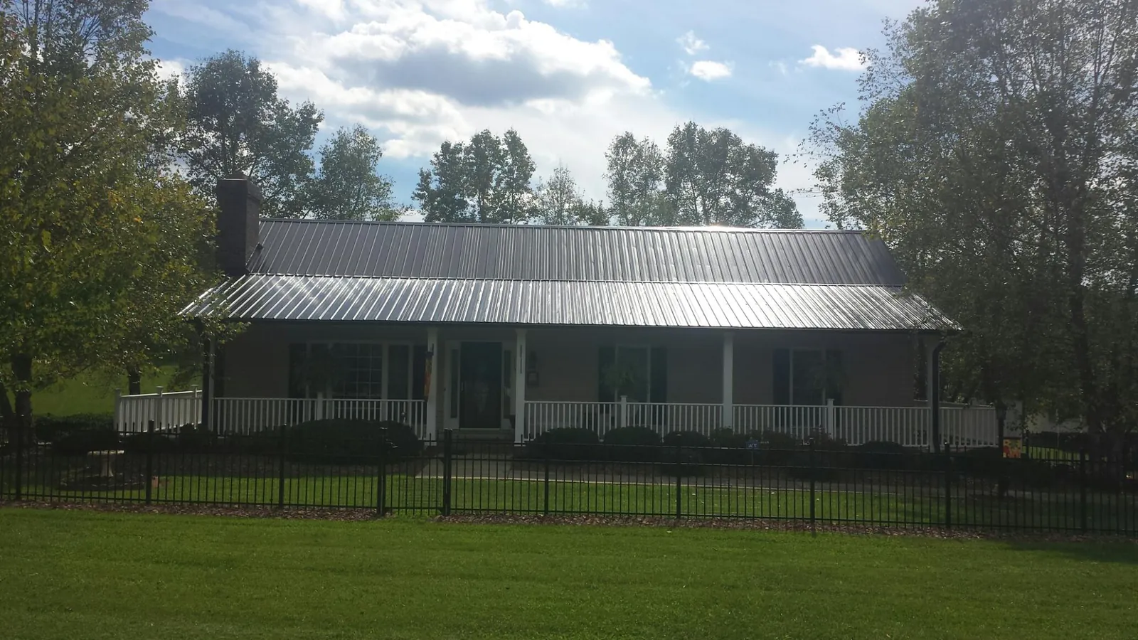 Gray metal roof on a brick ranch with a full width front porch — Gutter Guard Installation work by our crew in Otego