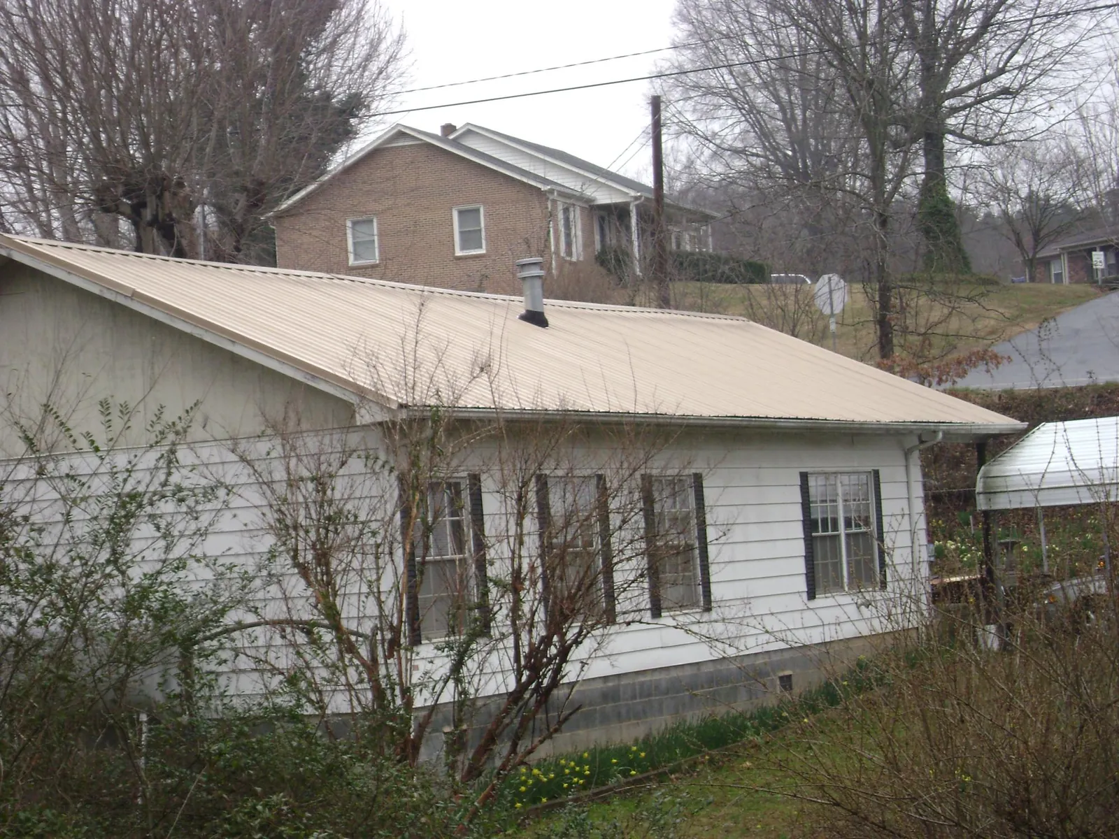 Tan metal roof on a white sided house set into a hillside — Commercial Roofing by Roofing Brothers in Otego