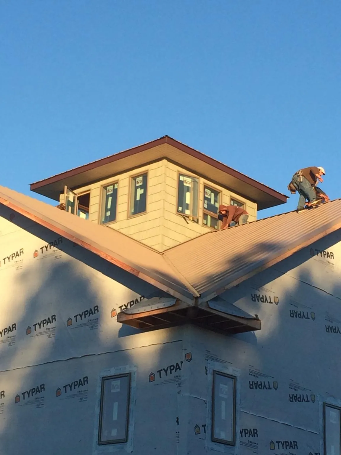 Roofers working around a rooftop cupola on a new metal roof at sunset — Roof Waterproofing in Otego by Roofing Brothers